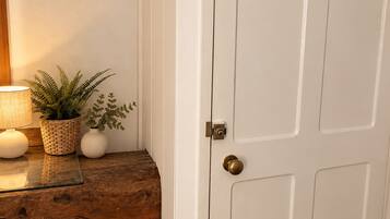 A white door with a brass doorknob, a wooden bench with a woven basket and potted plants, and a wall-mounted lamp.