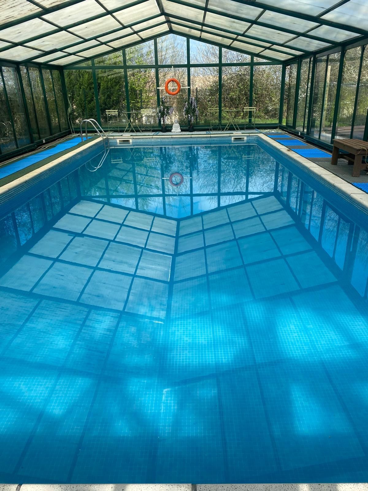 Una piscina interior d'aigua cristal·lina blava, envoltada d'una estructura de teulada de vidre.