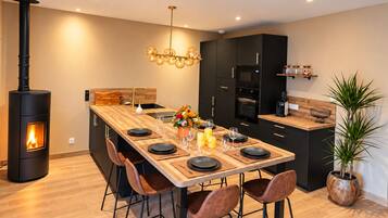 Une cuisine moderne dotée d’un îlot central, de meubles de couleur noire, d’un poêle à bois et d’un lustre.