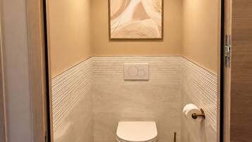 Ein modernes Badezimmer mit Toilette, Handtuchspender und einem gerahmten Kunstwerk an der Wand.
