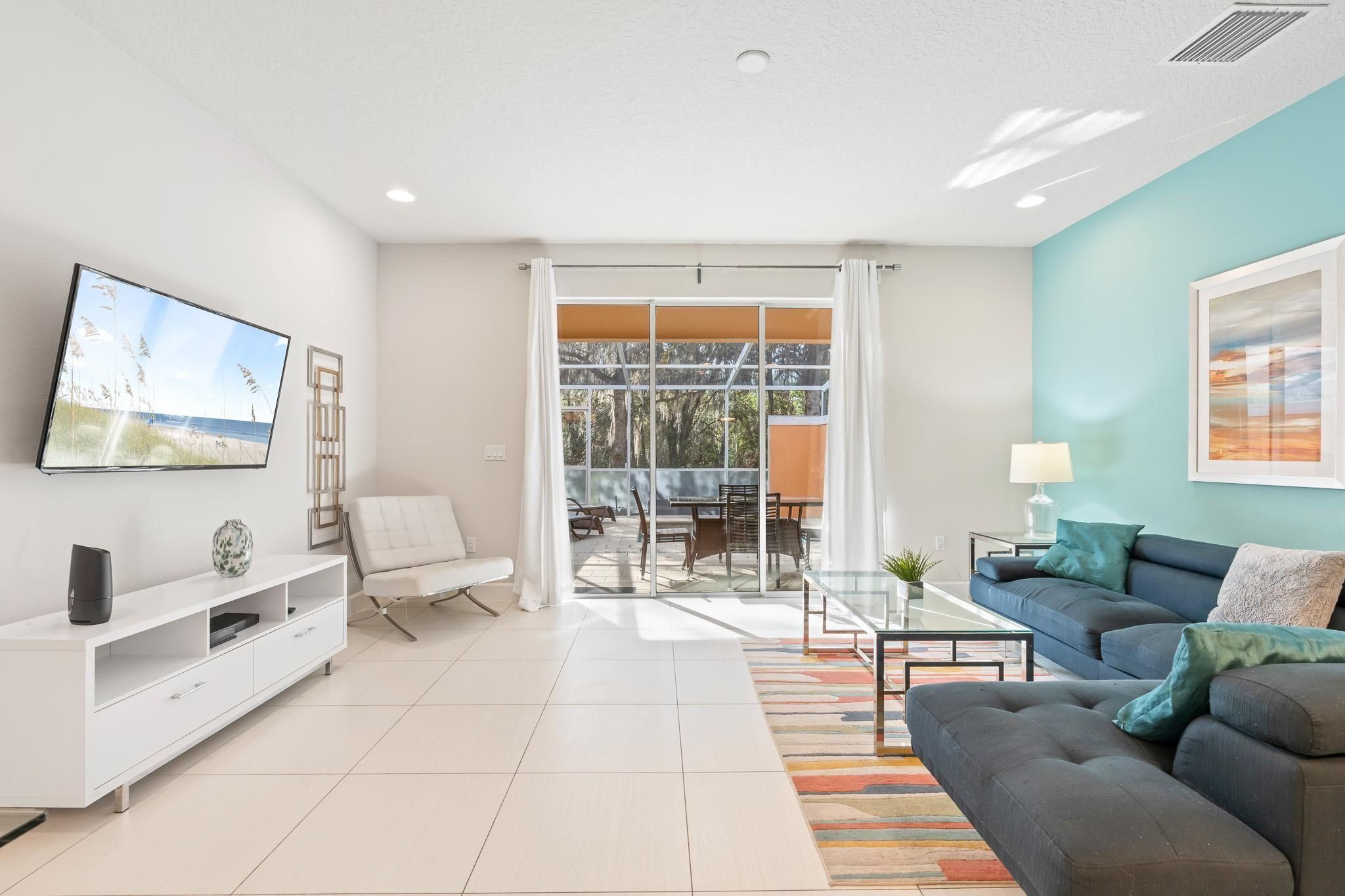 A modern living room with a flat-screen TV, a sofa, a coffee table, and a dining area with chairs and a table.