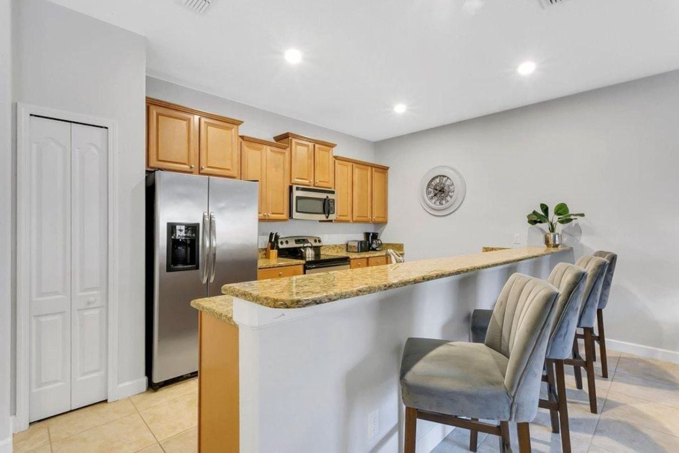 A kitchen with a central island, wooden cabinets, stainless steel appliances, and a clock on the wall.