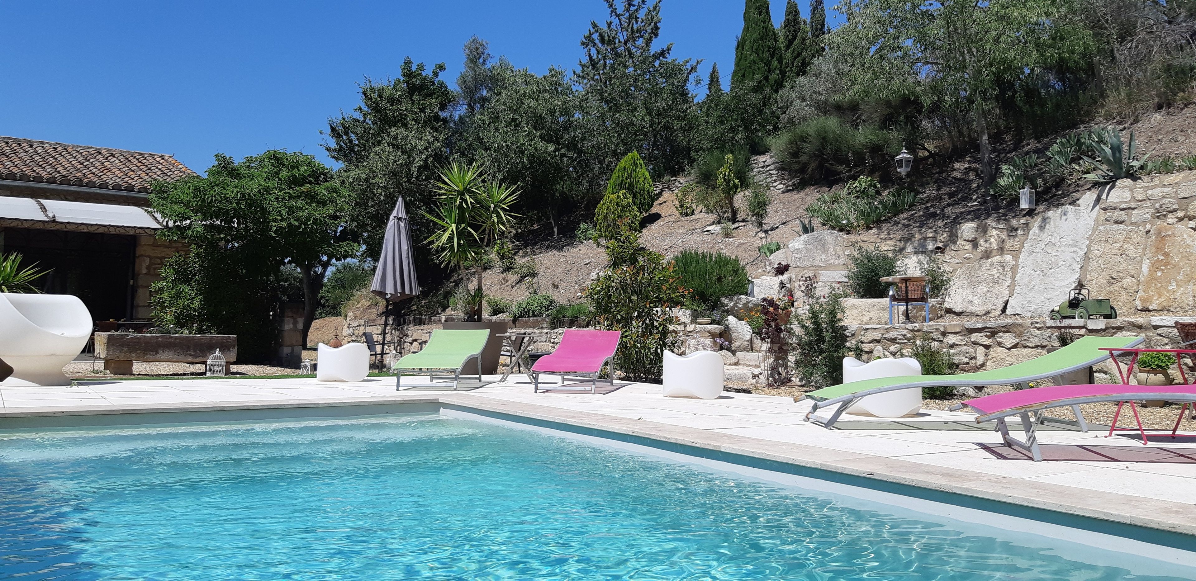 Ein Swimmingpool mit Liegestühlen und einer Steinmauer mit Bepflanzung.