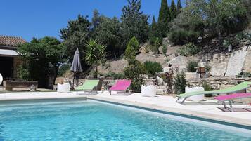 Ein Swimmingpool mit Liegestühlen und einer Steinmauer mit Bepflanzung.