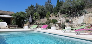 Ein Swimmingpool mit Liegestühlen und einer Steinmauer mit Bepflanzung.