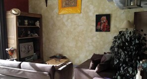 A living room with a sofa, a small table, a bookshelf, a framed picture, and a potted plant.