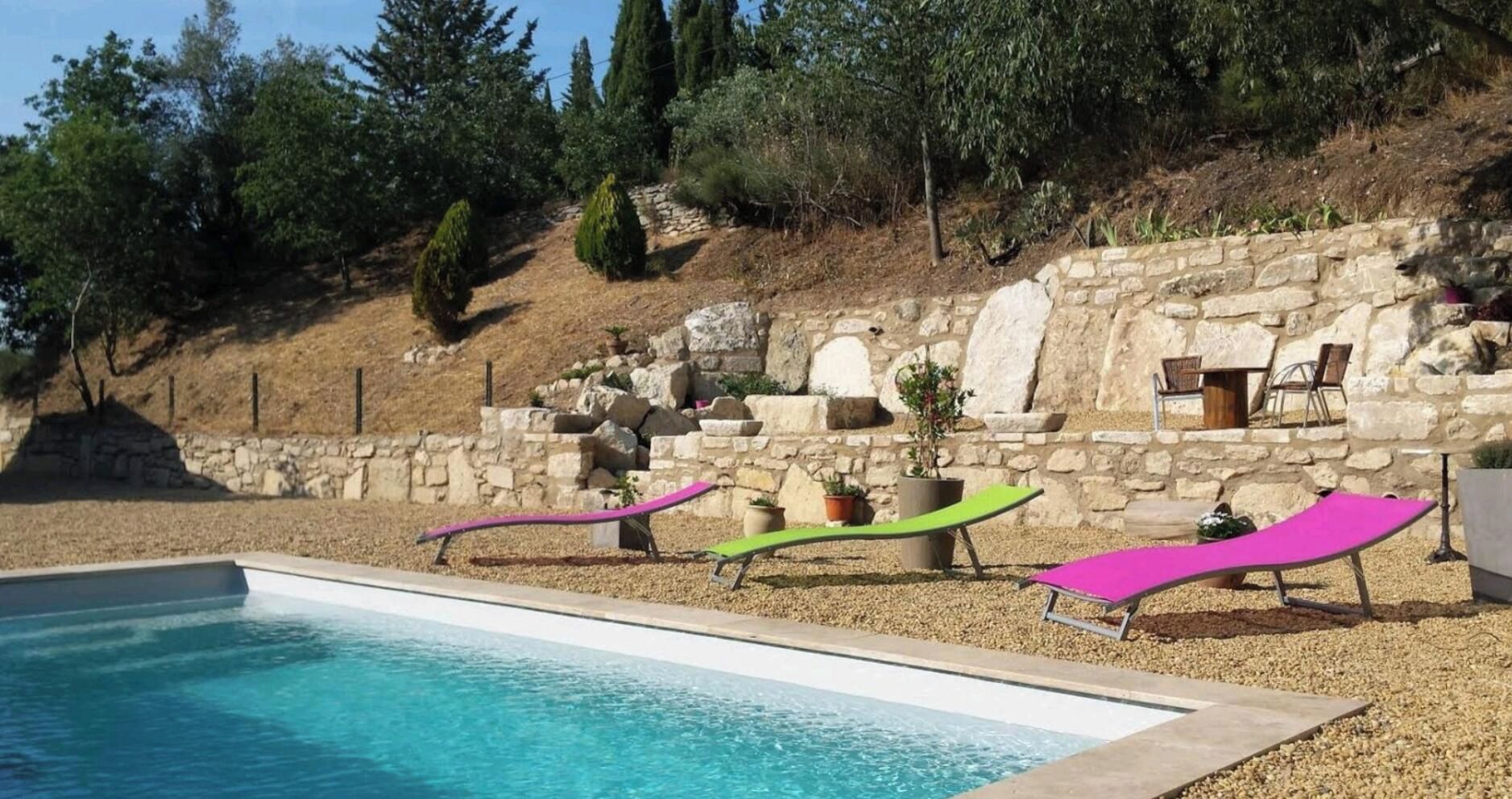 Piscina con sillas de descanso y un muro de piedra con plantas.