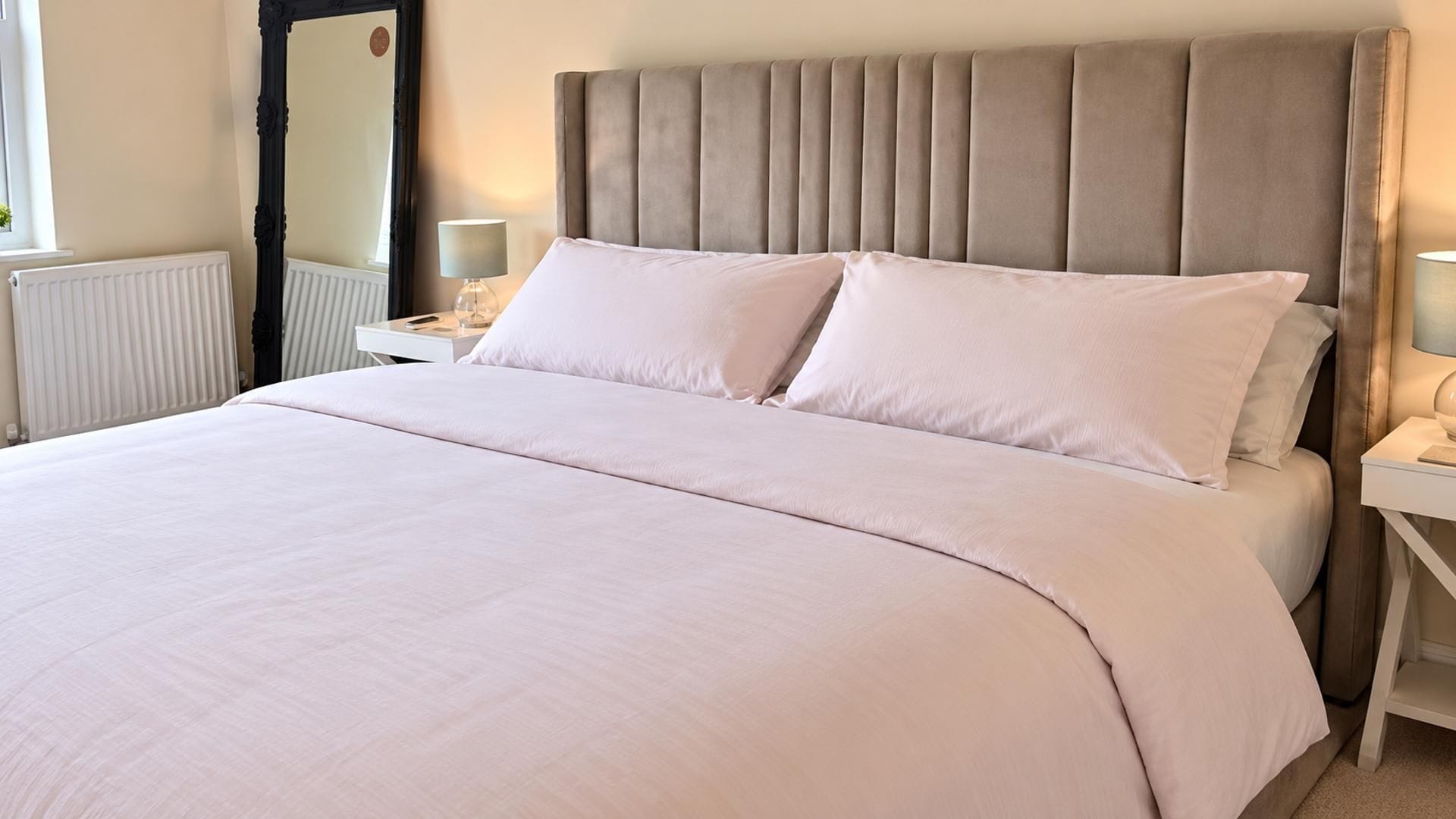 A neatly made bed with a headboard, two bedside tables with lamps, and a window with blinds.