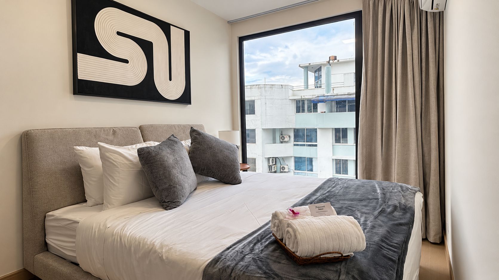 A hotel room with a large bed, a view of a building, and a window with curtains.