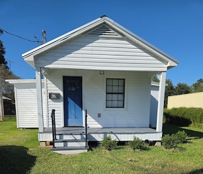 A small, single-story white building with a dark blue door and a small window.