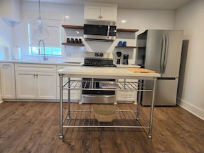 A modern kitchen with white cabinetry, stainless steel appliances, and a wooden floor.