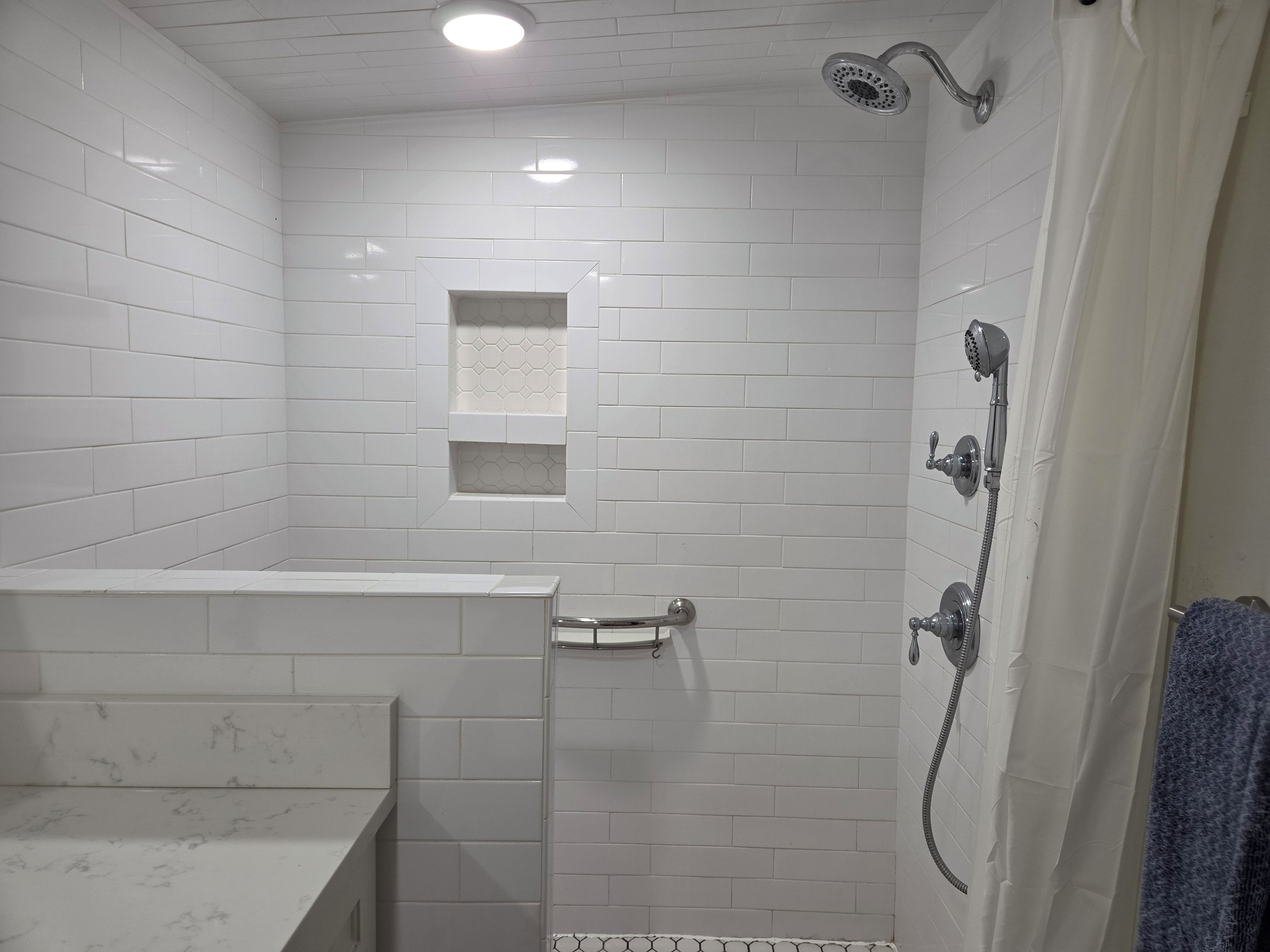 A bathroom with white subway tiles, a shower with a handheld showerhead, and a glass-enclosed toilet.