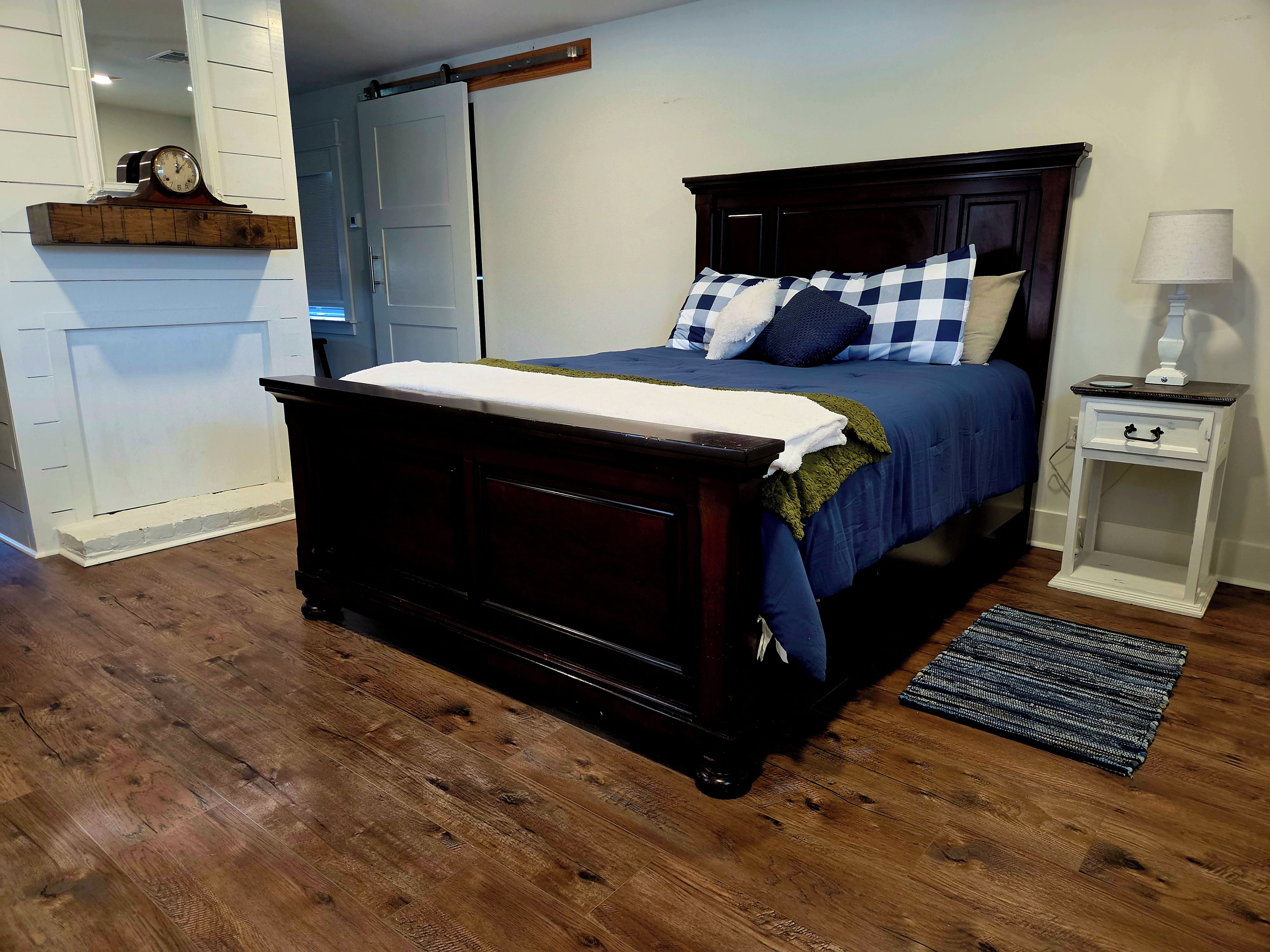 A bedroom with a dark wooden bed, a nightstand with a lamp, and a window with blinds.