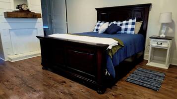 A bedroom with a dark wooden bed, a nightstand with a lamp, and a window with blinds.