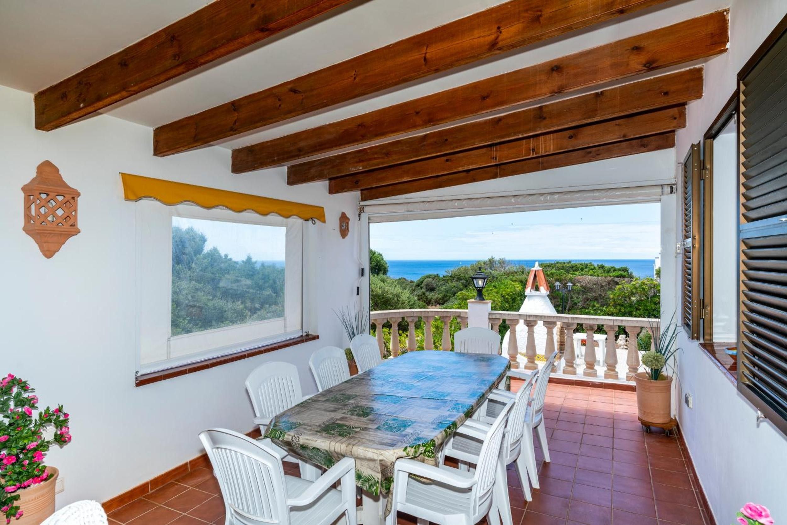 Une terrasse couverte avec une table et des chaises, une vue sur la mer et un plafond en bois.