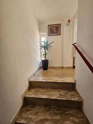 Un escalier orné d’un pot de fleurs en haut, un tableau accroché au mur et une rampe rouge.