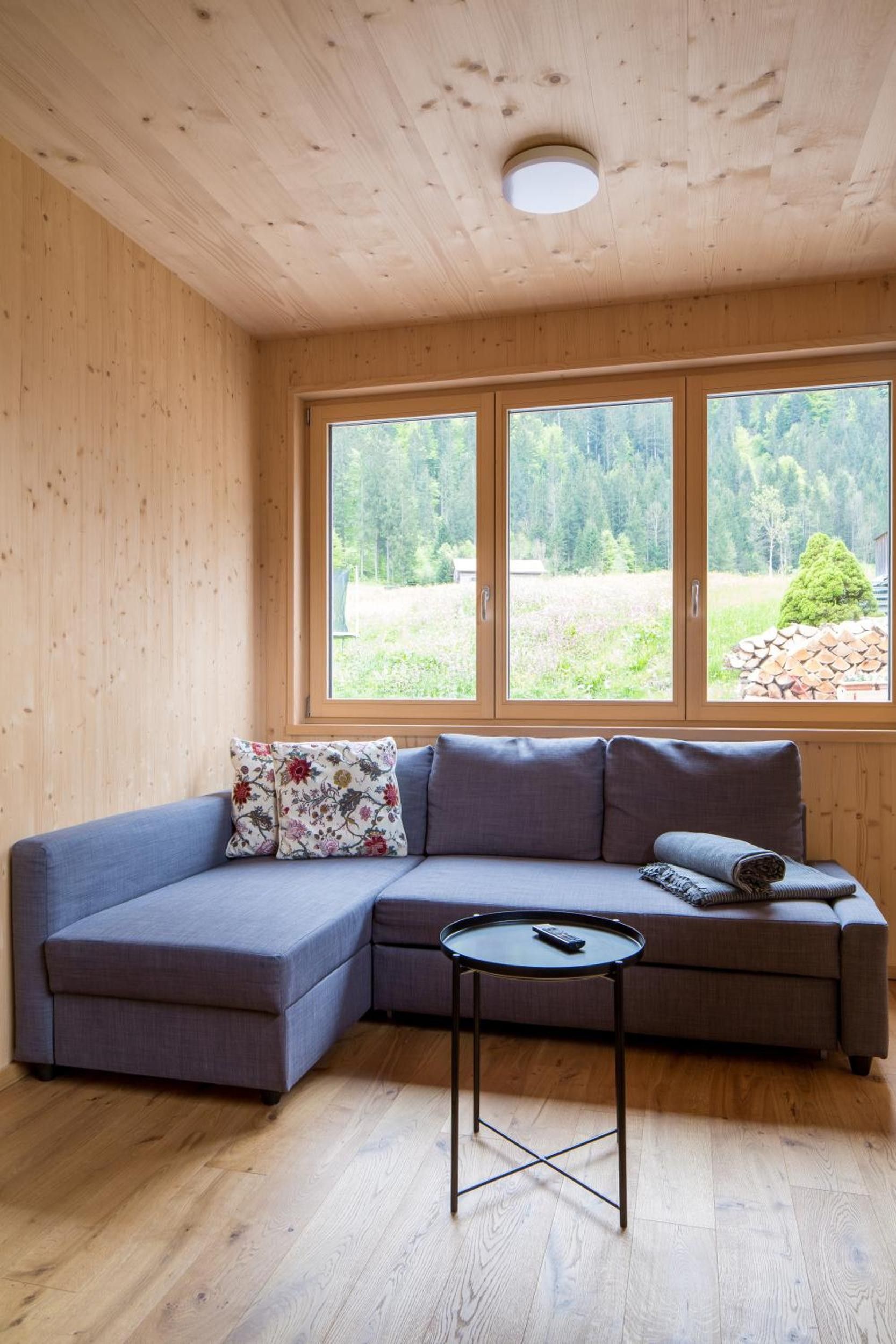 Ein Holzinnenraum mit einem Ecksofa, einem kleinen runden Tisch und einem großen Fenster mit Blick auf Grünflächen.