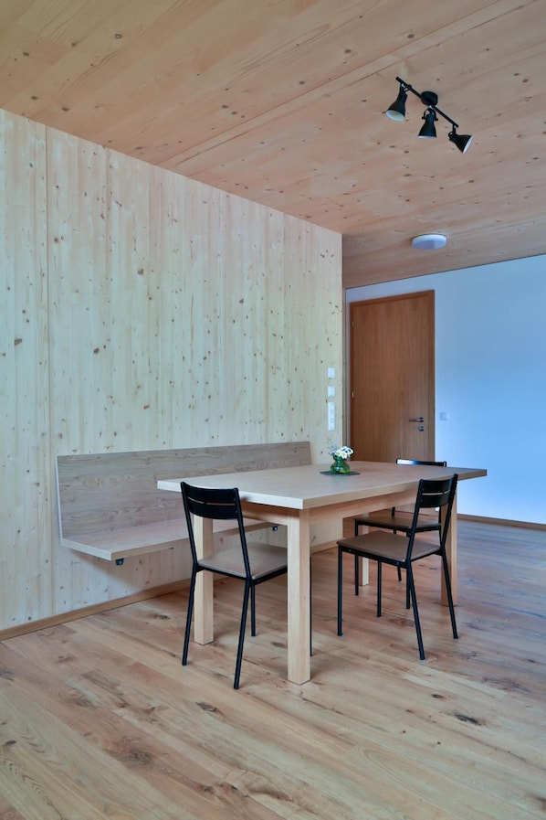 Een strak ingerichte eethoek met een houten tafel en stoelen, een bankje, en een houten plafond met een lamp.