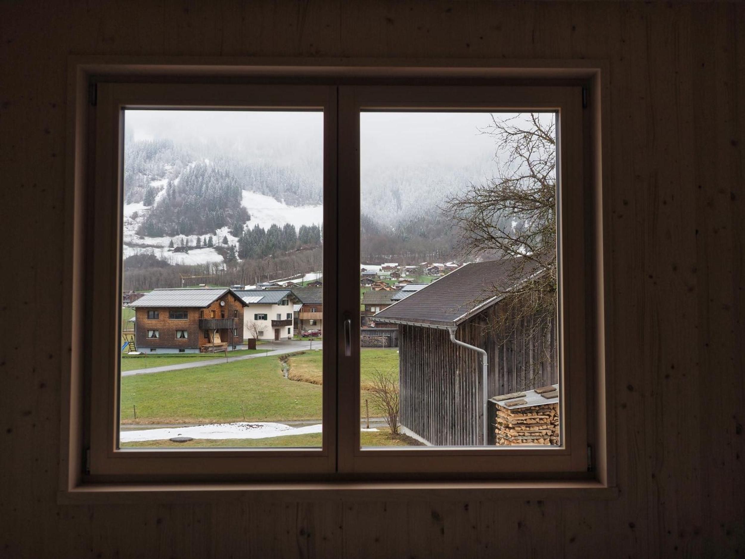 Ein Fenster mit Blick auf eine verschneite Landschaft, Gebäude und eine Holzkonstruktion.