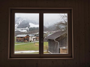 Een raam met uitzicht op een besneeerd landschap, gebouwen en een houten constructie.
