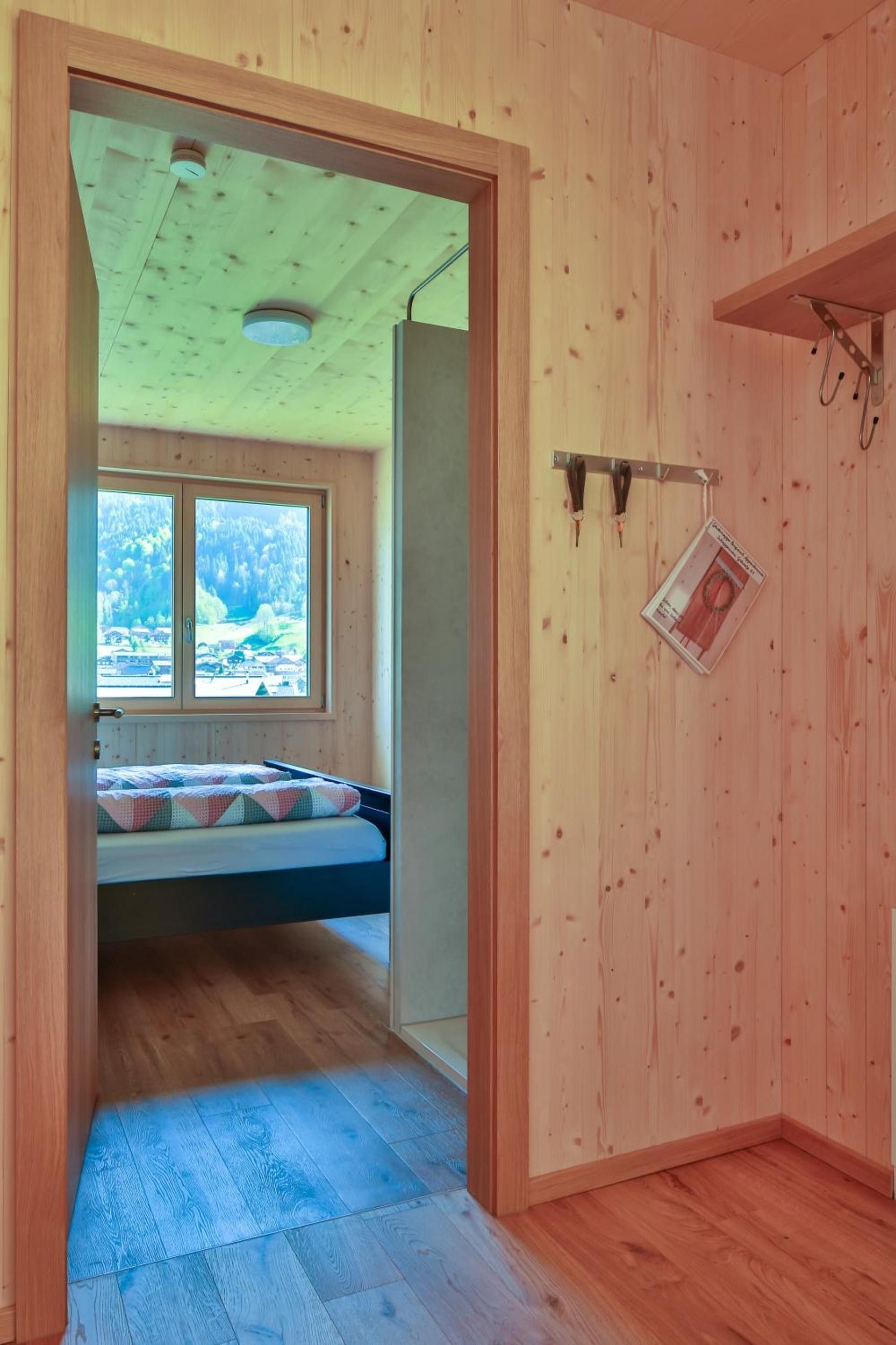 Ein Zimmer mit Holzboden, einem Bett, einem Fenster und einer Tür zu einem weiteren Raum.