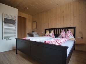 Ein Schlafzimmer mit Holzboden, einem Bett mit schwarzem Gestell, einem Nachttisch und einem Spiegel.