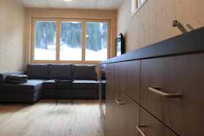 Een modern interieur met een modulaire bank, houten kasten en een groot raam met uitzicht op bomen.