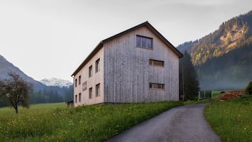 Ein Holzhaus mit geneigtem Dach, einer gepflasterten Auffahrt und einer Bergkulisse im Hintergrund.
