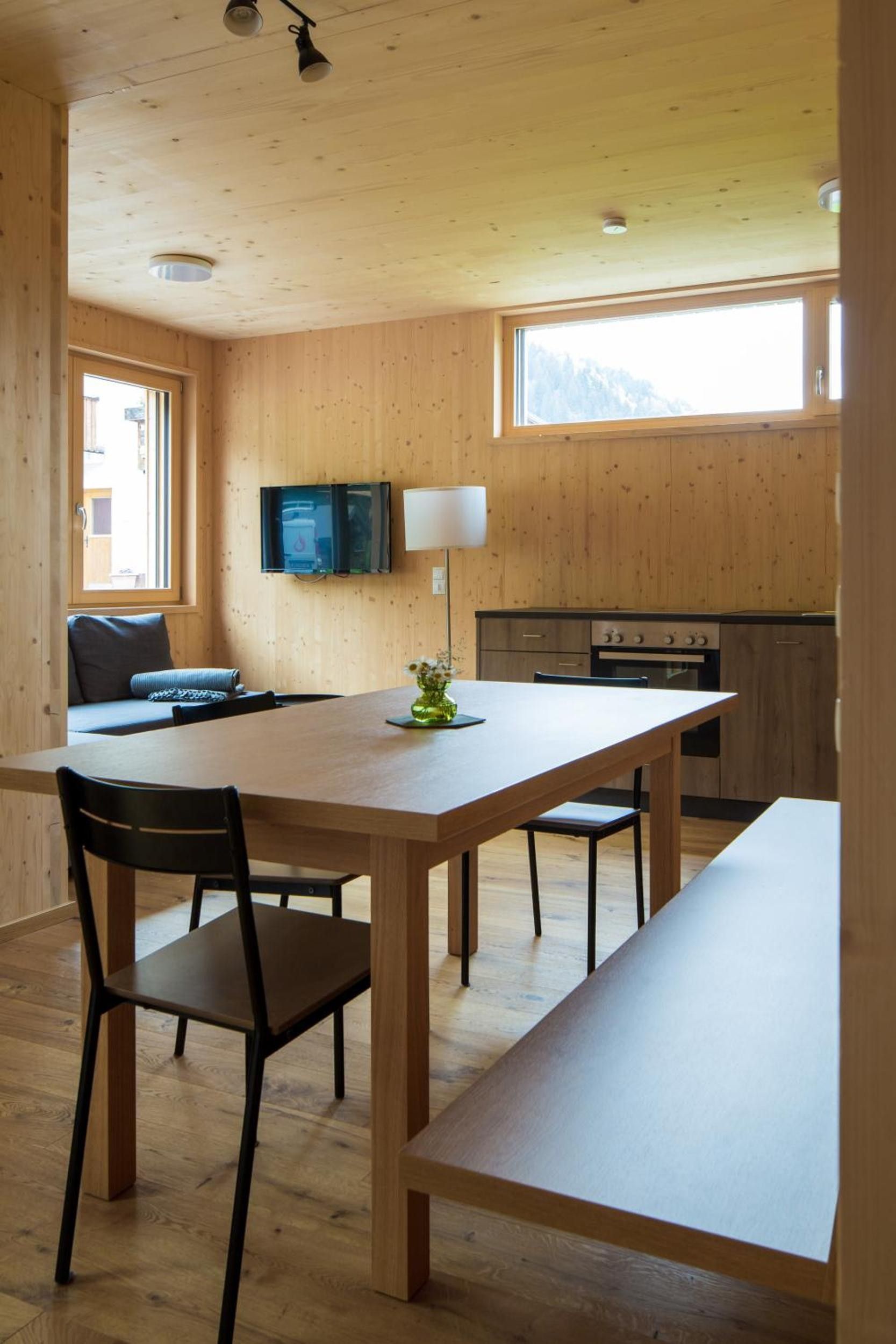 Ein Holzinterieur mit Esstisch, Stühlen, einem an der Wand befestigten Fernseher und einer Küchenzeile mit Herd.
