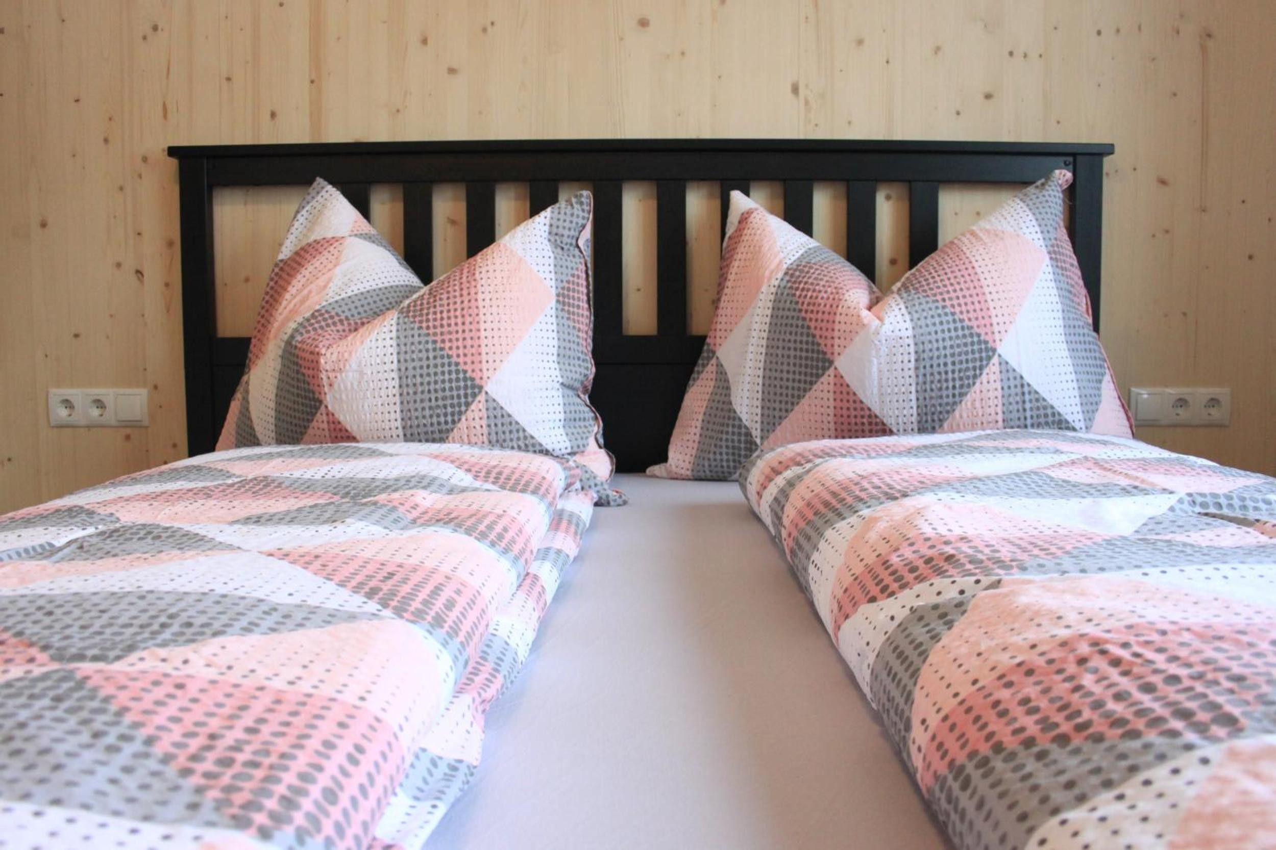 Ein Zimmer mit zwei Betten, jedes mit einem gemusterten Überwurf und passenden Kissen, an einer Holzwand.
