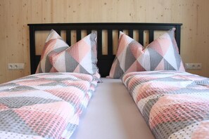 Une chambre avec deux lits, chacun recouvert d’une couvre-lit à motifs et agrémenté d’oreillers assortis, le tout adossé à un mur en bois.