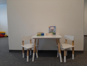 Ein kleiner weißer Tisch mit zwei hölzernen Stühlen, einem Kinderbuch und einem Spielzeugauto.