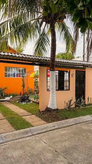 Um pequeno edifício térreo com telhado de cerâmica, uma palmeira em frente e um caminho de entrada pavimentado.
