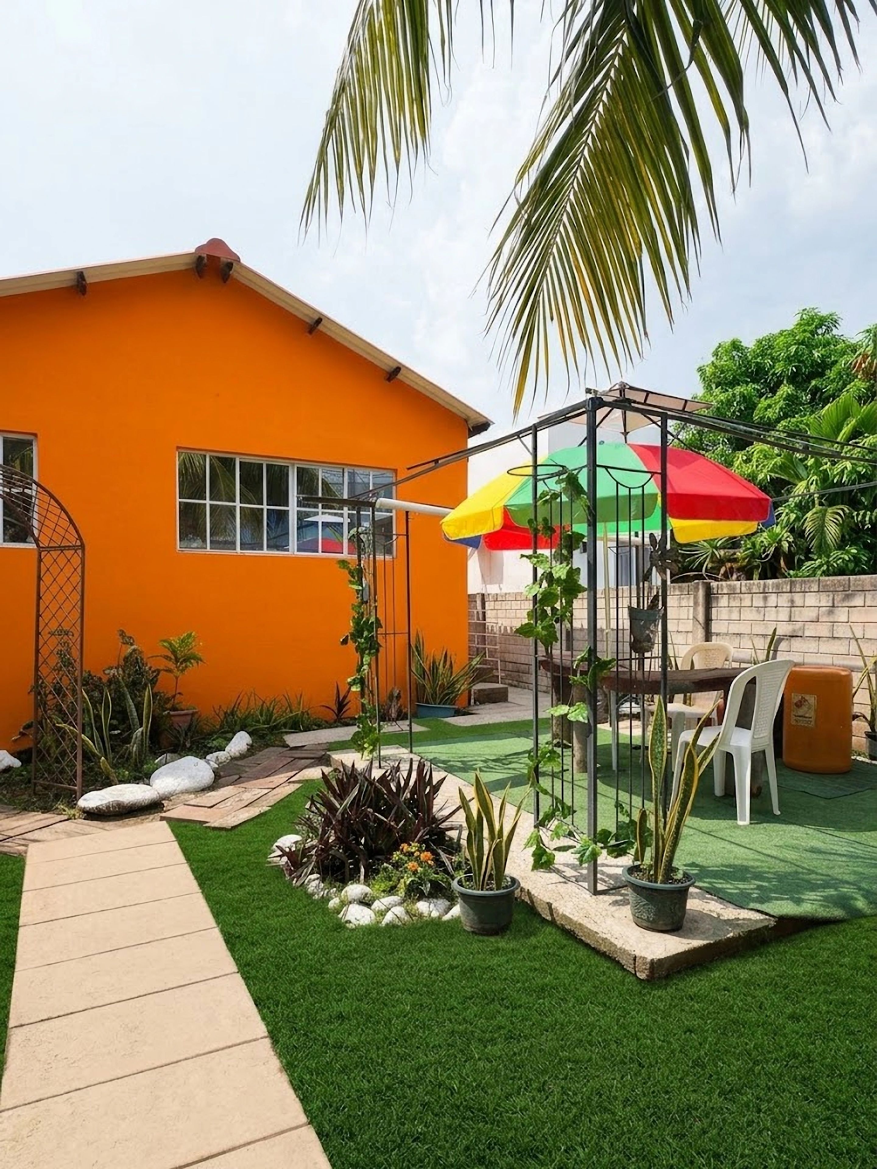Una propiedad residencial con un césped cuidado, un patio con mobiliario exterior y un paraguas llamativo.