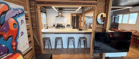 Una cocina moderna con una isla central, taburetes de bar y un televisor grande.