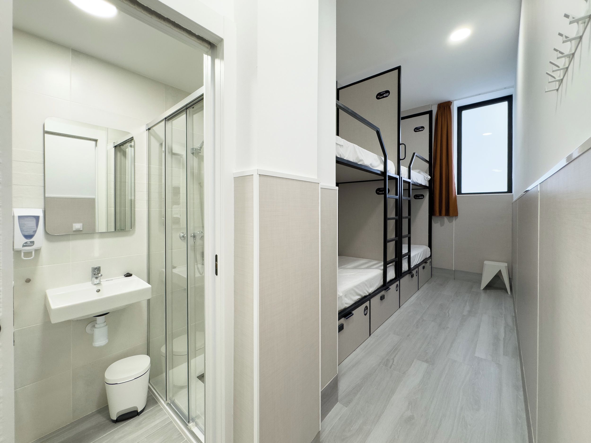 Quarto de hotel pequeno com chuveiro, vaso sanitário e beliche.
