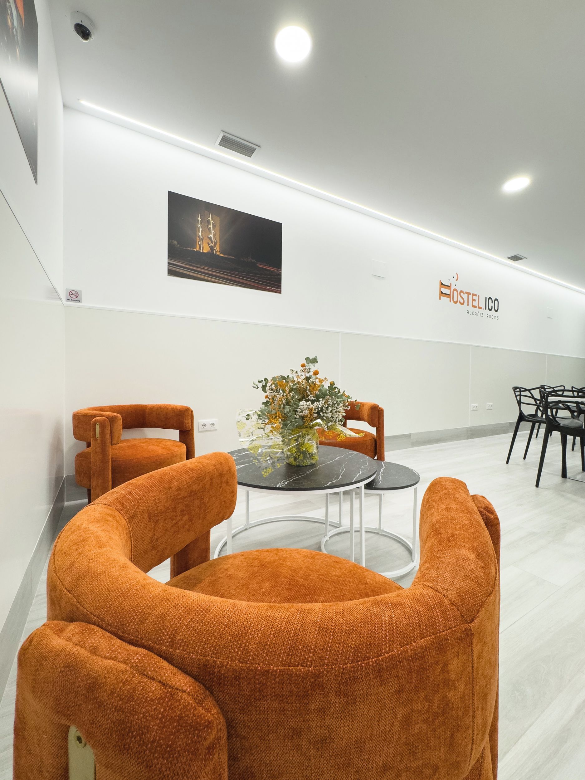 Un interior moderno con una mesa redonda, sillas naranjas, un florero con flores y un letrero en la pared.