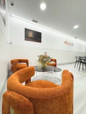 A modern interior with a round table, orange chairs, a vase with flowers, and a wall-mounted sign.