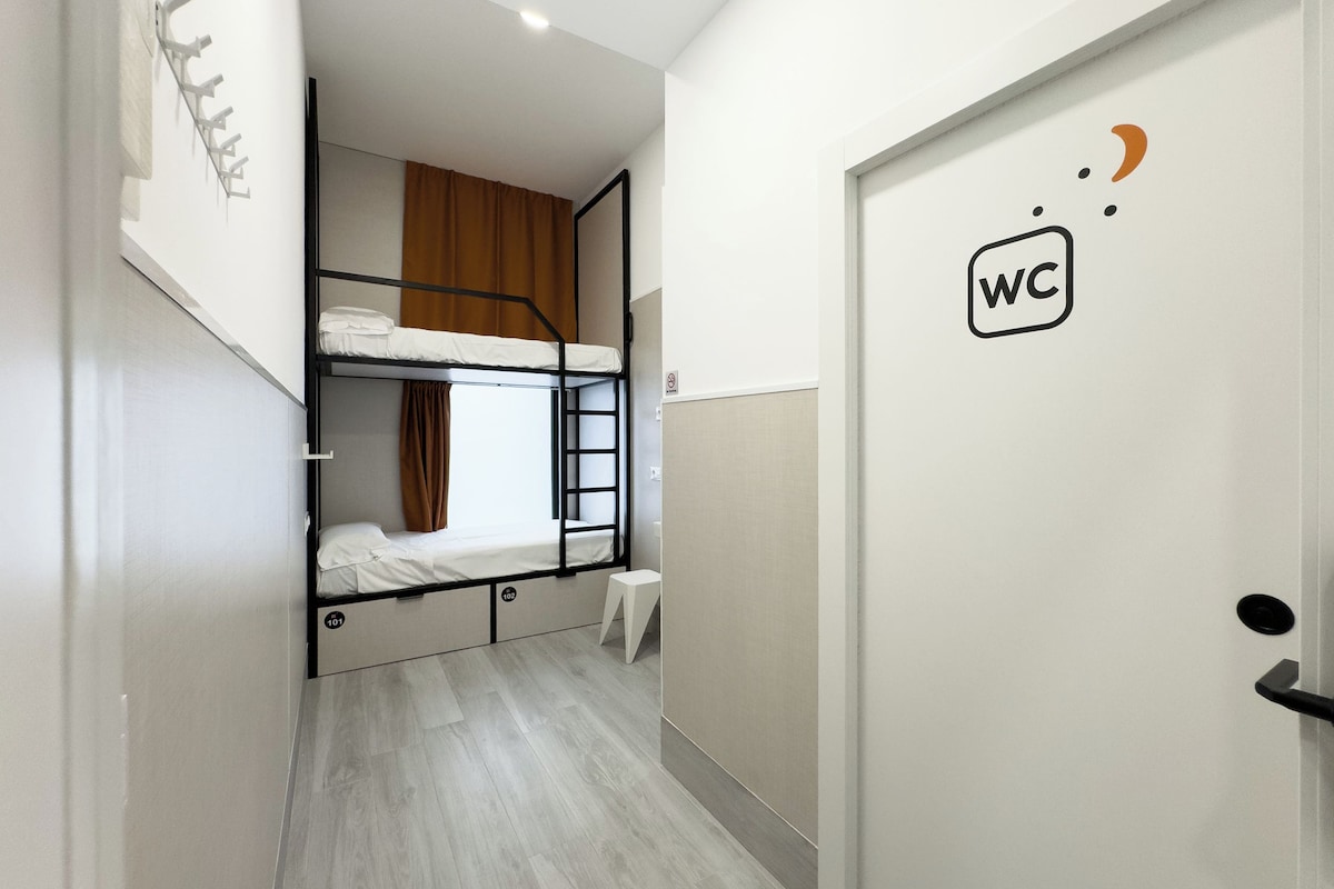 A corridor with bunk beds, a WC sign, and a small stool.