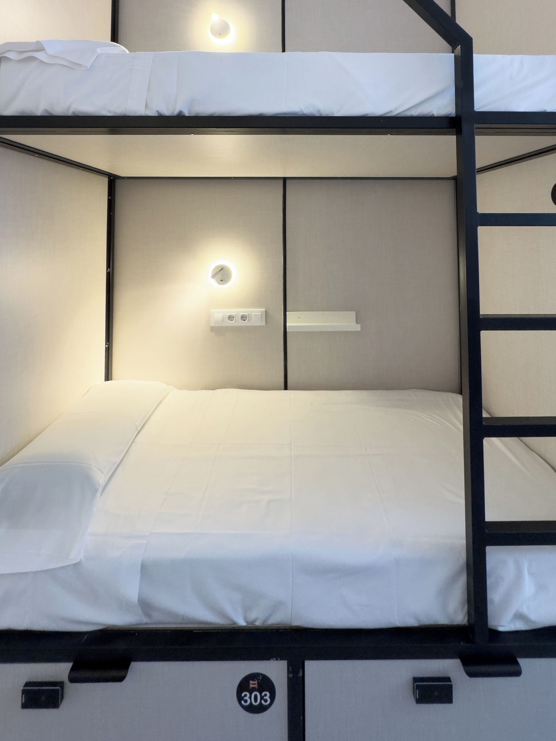 A bunk bed with a headboard, a wall-mounted light, and a small shelf.