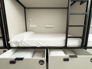 A bunk bed room with a white mattress, a wall-mounted light switch, and a door with a black handle.