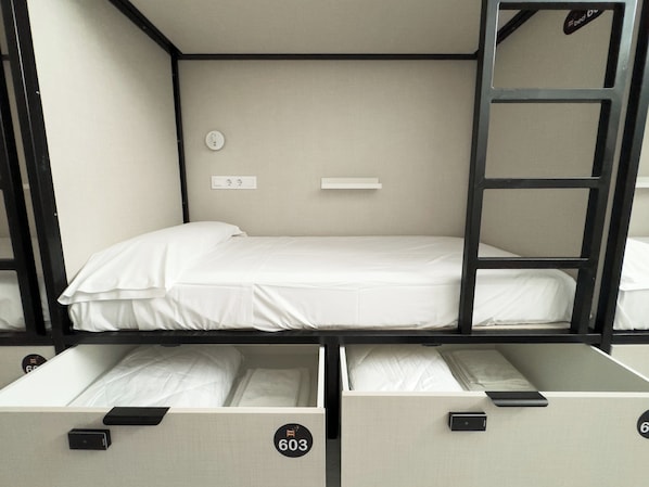 A bunk bed room with a white mattress, a wall-mounted light switch, and a door with a black handle.