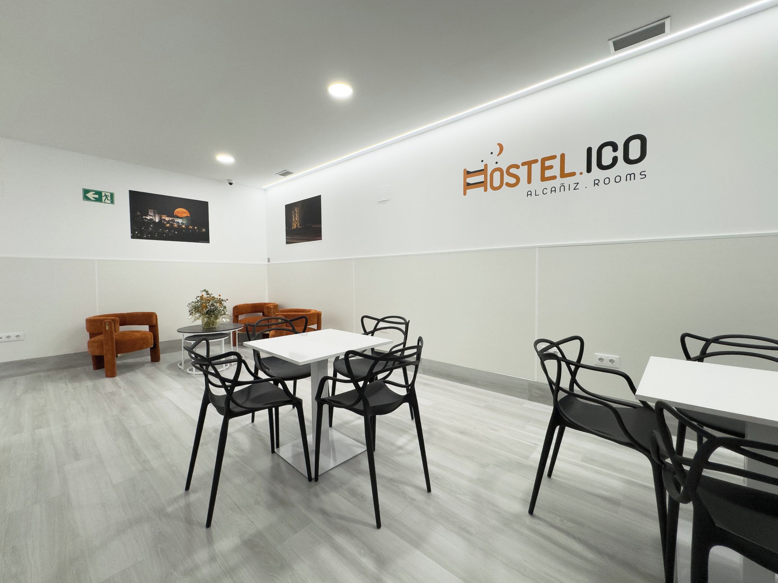 A modern hostel room with a white wall, a logo, and a wooden floor.