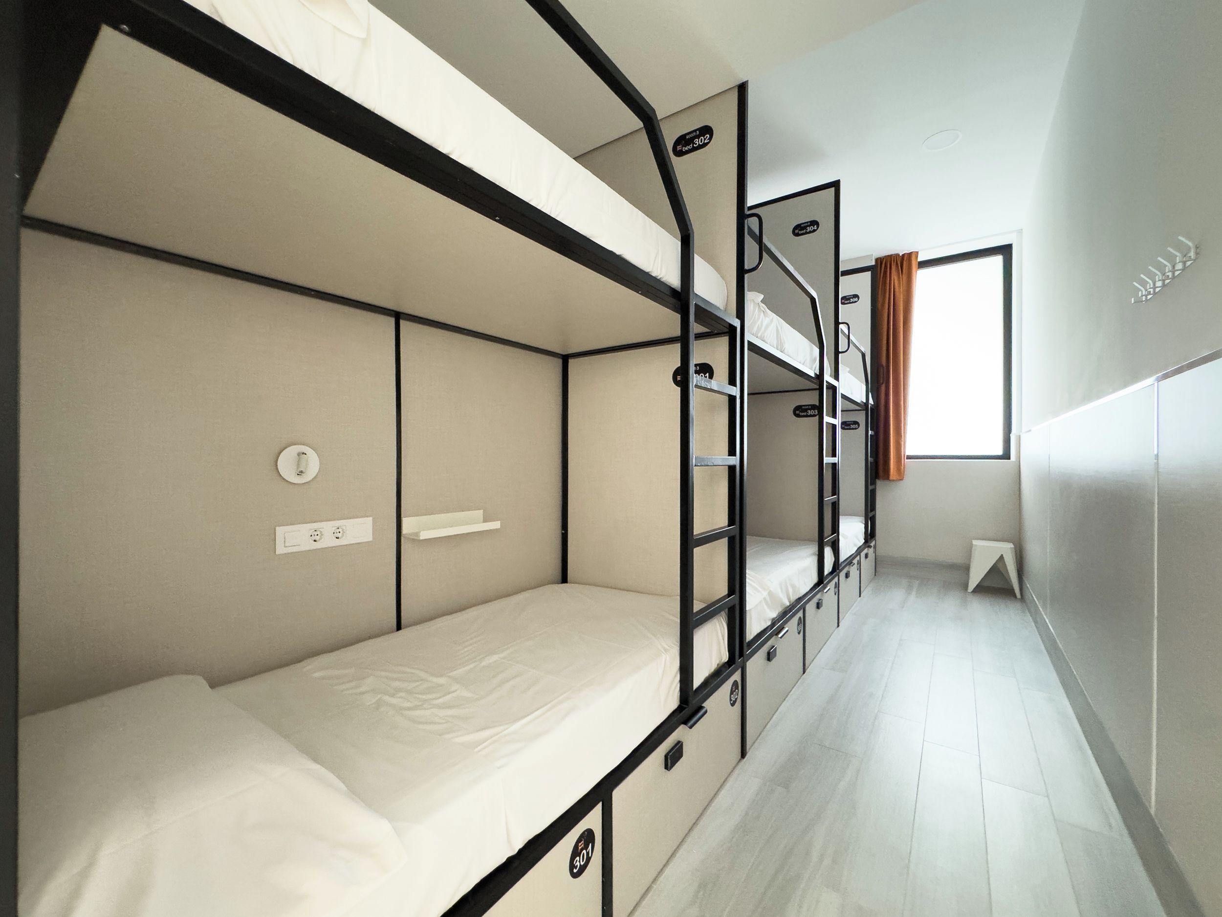 A bunk bed room with a window, a small stool, and a wall-mounted light fixture.