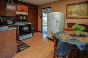 Una cocina con armarios de madera, microondas, horno y refrigerador. Hay una mesa de comedor con individuales y una planta en maceta.