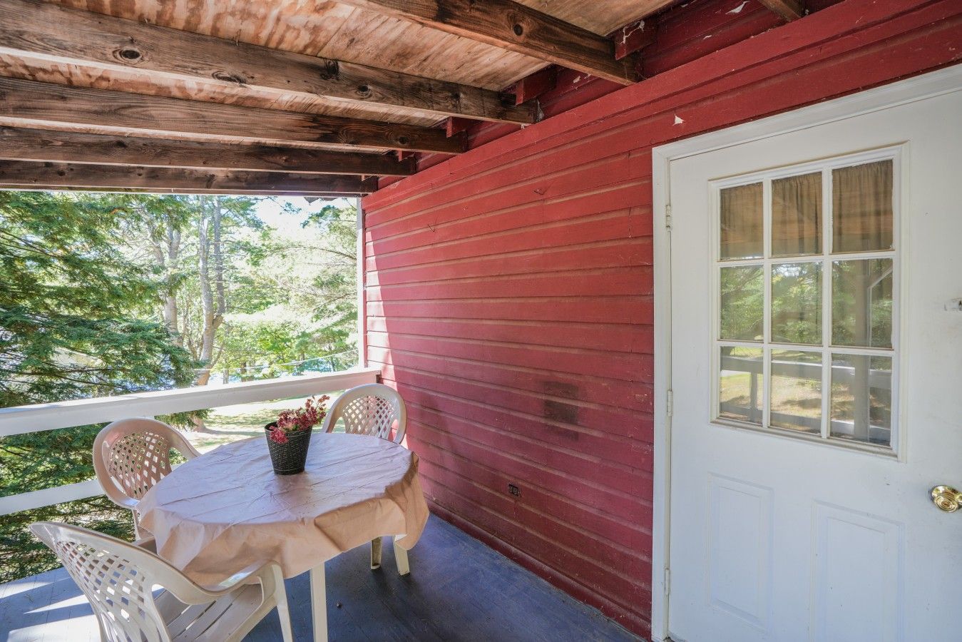 Un porche cubierto con una pared exterior roja, una puerta blanca y una mesa con sillas.