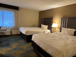 Una camera d'albergo con due letti, un termosifone e una finestra con tende.