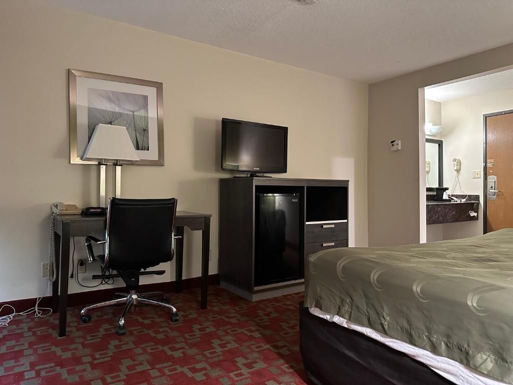 A hotel room with a bed, a desk with a chair, a television, and a framed picture on the wall.