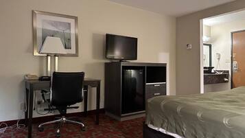 A hotel room with a bed, a desk with a chair, a television, and a framed picture on the wall.