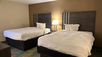 A hotel room with two beds, a nightstand with a lamp, and a carpeted floor.